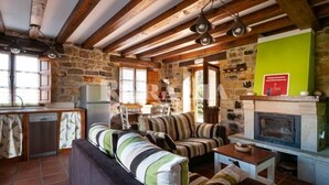 A rustic interior with a stone wall, wooden beams, a fireplace, and a sofa set. - Casa Ángela - country house in Villanueva de la Peña (Cantabria) | 6 guests (Villanueva De La Peña)