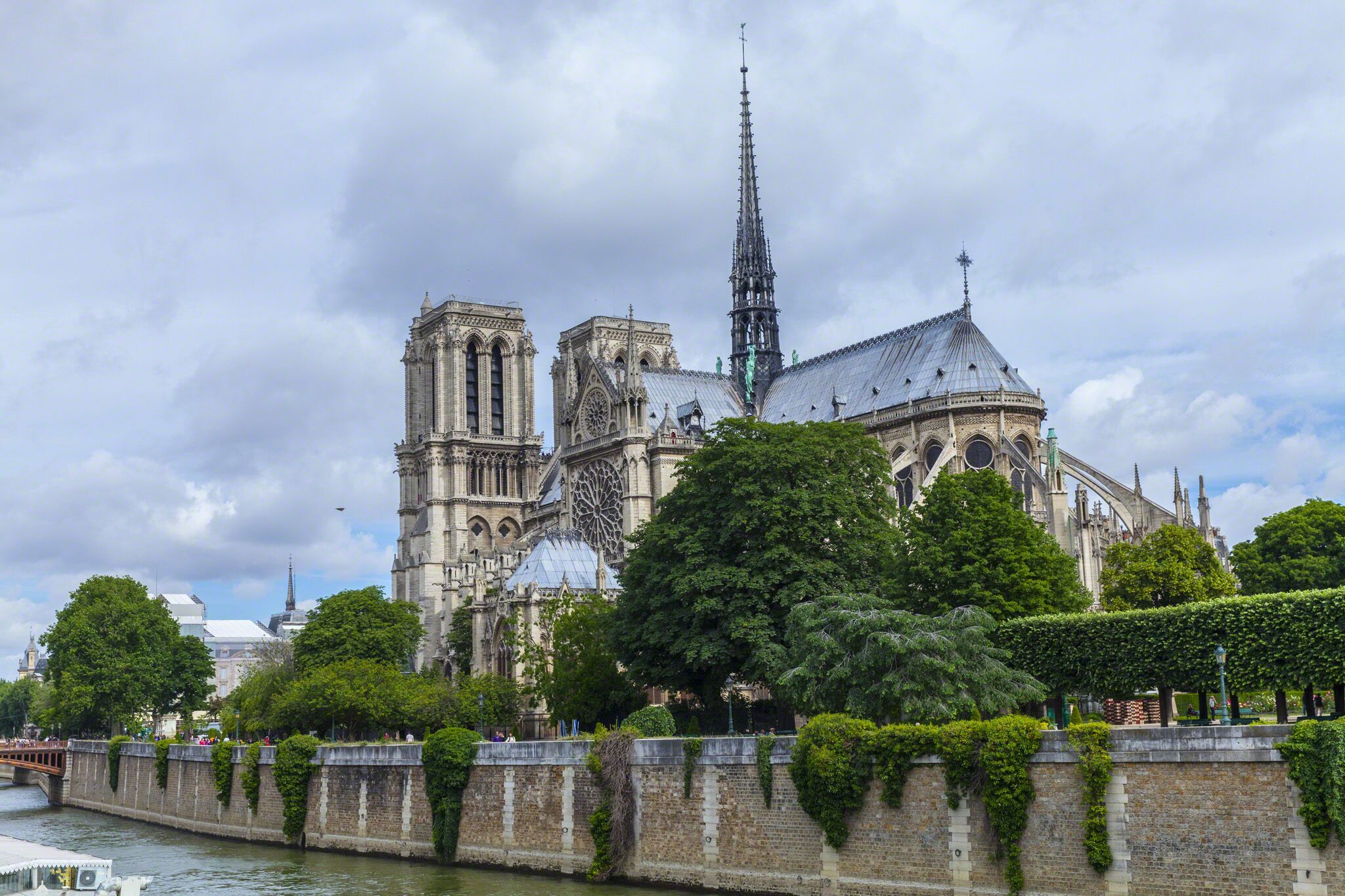 A historic cathedral with twin towers and a spire, surrounded by lush greenery and a river.