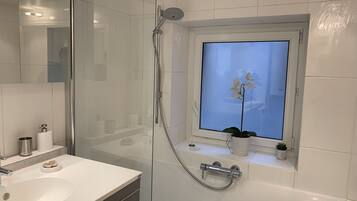 Une salle de bain moderne avec une douche en verre, un lavabo blanc et une fenêtre ornée d’une orchidée en pot.