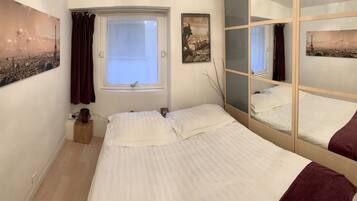 Een slaapkamer met een bed, een raam met gordijnen, een spiegel en twee ingelijste foto's aan de muur.