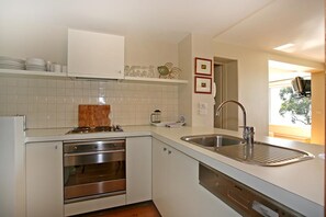 A modern kitchen with white cabinetry, a stainless steel sink, and a built-in oven. - Apartment 7 Kalimna (Lorne)