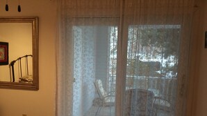 Ett sovrum med en säng, ett fönster med tunna, genomskinliga gardiner, en stol och utsikt över omgivningen.