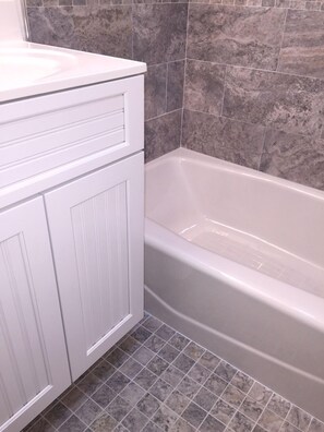 A bathroom with a white vanity, a bathtub, and grey marble tiles.