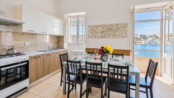 A modern kitchen with a dining area, large windows, and a view of the sea.