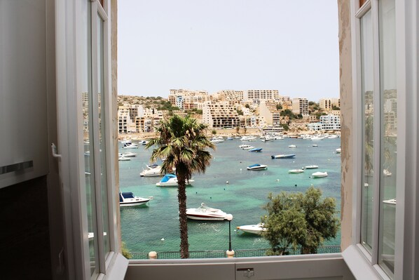 Une vue depuis une fenêtre donnant sur une marina, avec des bateaux, un palmier et des bâtiments en arrière-plan.