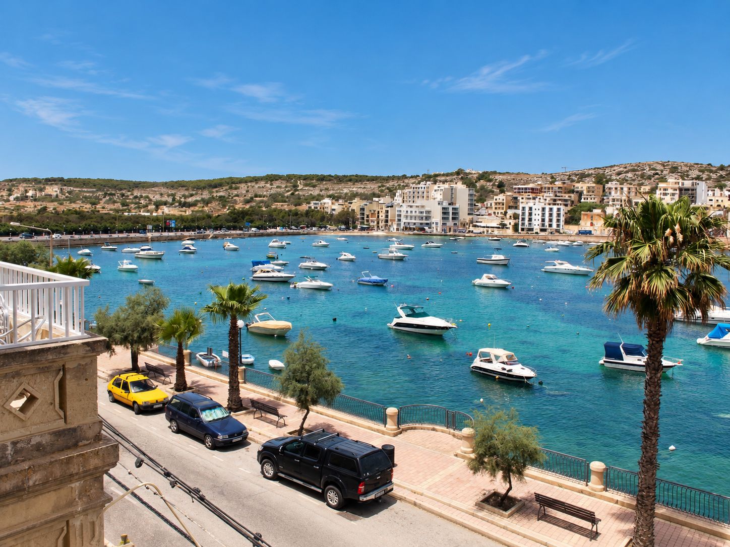 Un puerto deportivo con barcos, una carretera con coches y edificios al fondo.