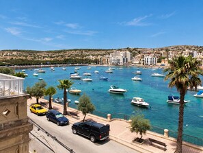 A marina with boats, a road with cars, and buildings in the background. - BH2 - Seafront 3 bedroom apt. - St Paul`s Bay, Back Terrace, (San Pawl il-Bahar)
