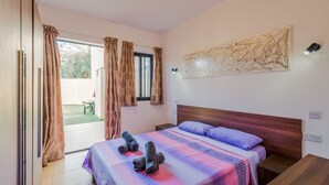 A bedroom with a bed, a wooden headboard, a nightstand, a table, and a window with curtains. - BH2 - Seafront 3 bedroom apt. - St Paul`s Bay, Back Terrace, (San Pawl il-Bahar)