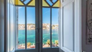 A room with a large window overlooking a body of water and a cityscape. - BH2 - Seafront 3 bedroom apt. - St Paul`s Bay, Back Terrace, (San Pawl il-Bahar)