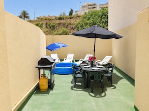Une terrasse extérieure avec une table ronde, des chaises, un barbecue, une piscine gonflable et une bouteille de gaz.