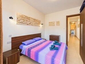 Une chambre à coucher avec une tête de lit en bois, un lit recouvert d’une couvre-lit à motifs, une table de chevet, une commode et des œuvres d’art murales.