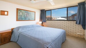 Une chambre à coucher avec un grand lit, une table de chevet, une lampe, un tableau et une fenêtre avec des rideaux.