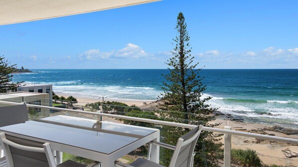 Ein Balkon mit freiem Blick auf den Ozean, einen Sandstrand und eine hohe Kiefer.