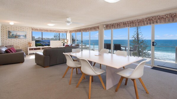 A spacious living area with a large dining table, comfortable seating, and a view of the ocean.