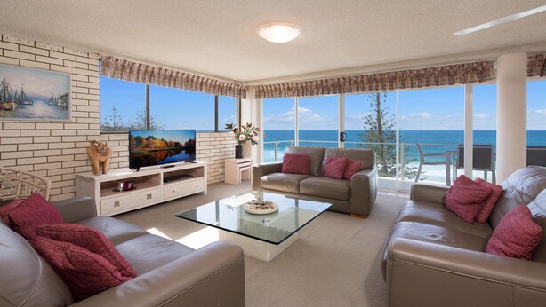 Un salon doté d’une grande fenêtre donnant sur la mer, d’un téléviseur à écran plat, d’un canapé et d’une table basse.