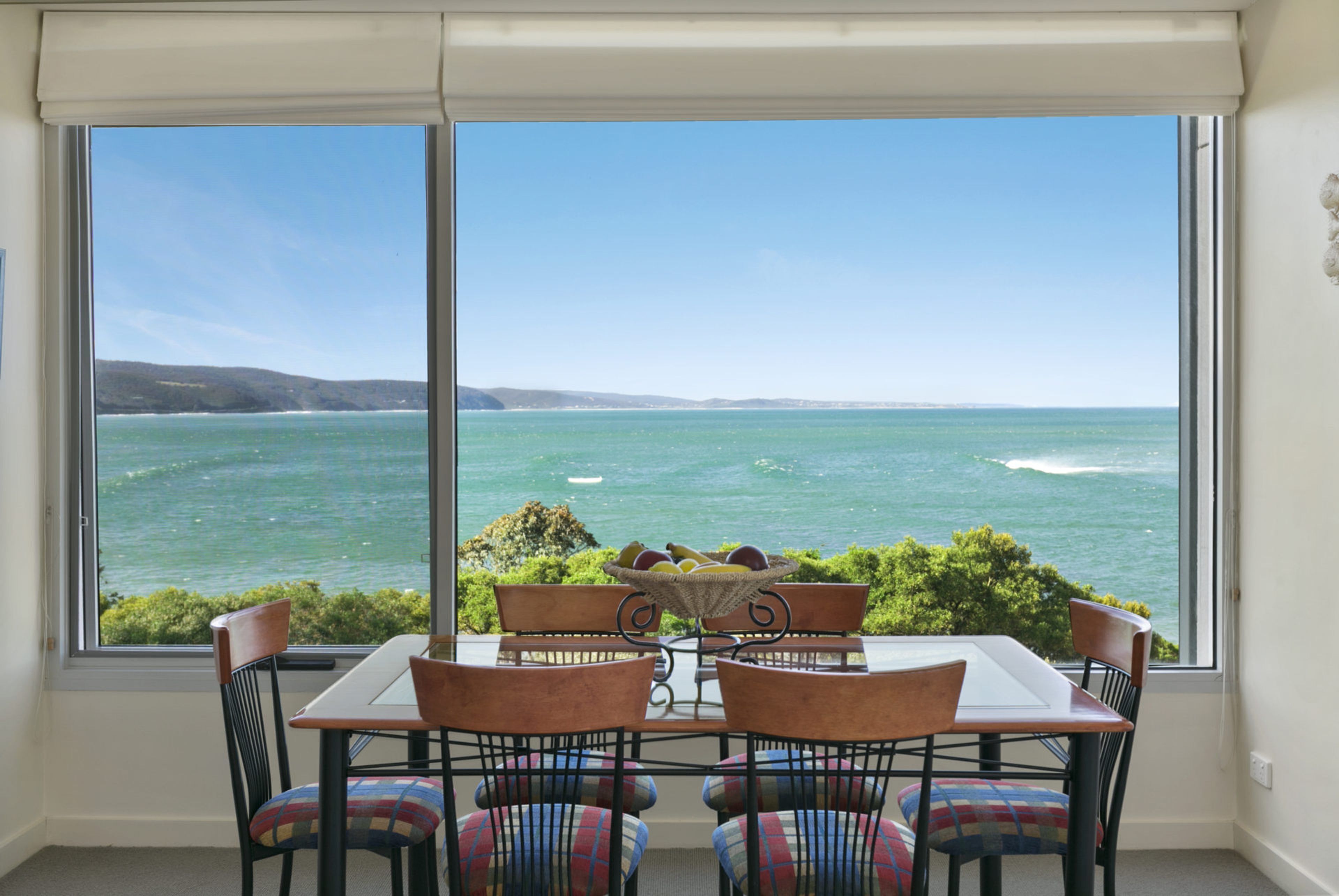 A dining area with a table and chairs facing a large window overlooking a body of water.