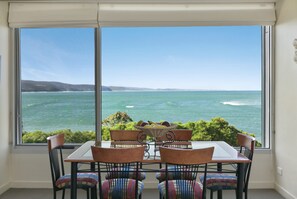 A dining area with a table and chairs facing a large window overlooking a body of water.