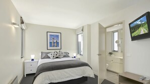 A bedroom with a bed, bedside tables, a nightstand, a dresser, a mirror, and a television. - Apartment 9 Kalimna (Lorne)