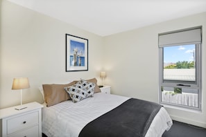 A bedroom with a bed, two bedside tables, a window, and a framed picture on the wall.