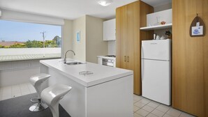 A modern kitchen with a central island, white cabinetry, and a view of the outside. - Apartment 9 Kalimna (Lorne)