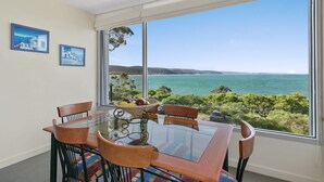 A dining area with a glass table, chairs, and a view of the sea. - Apartment 9 Kalimna (Lorne)