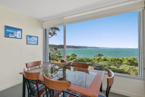 A dining area with a glass table, chairs, and a view of the sea.