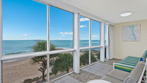 A room with large windows overlooking a beach, a map on the wall, and a striped sofa. - Culverston Unit 15 Kings Beach QLD (KINGS BEACH)