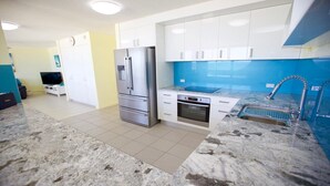 A modern kitchen with white cabinets, a stainless steel refrigerator, a built-in oven, and a blue backsplash. - Culverston Unit 15 Kings Beach QLD (KINGS BEACH)