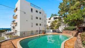 A modern building with a pool, surrounded by a white fence and palm trees.