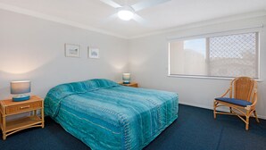 A bedroom with a bed, two bedside tables with lamps, a chair, a window with a view, and a ceiling fan.
