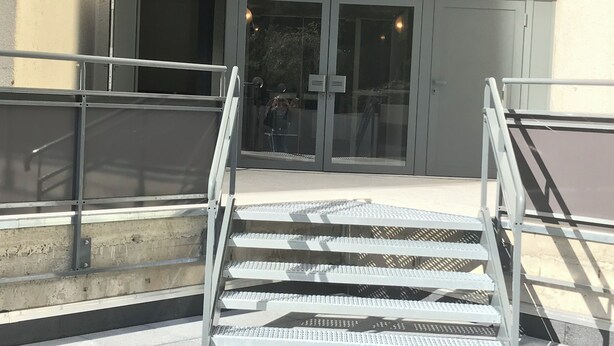 Un juego de escaleras de metal que conducen a la entrada de un edificio con puertas de cristal y barandilla de metal.