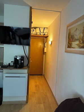 Una cocina compacta con cafetera, un refrigerador pequeño y un televisor sobre la encimera.