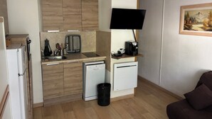 A compact kitchen with wooden cabinets, a built-in dishwasher, a coffee machine, and a flat-screen TV. - Studio - BAREGES (Bareges)