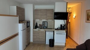 A compact kitchen with a microwave, refrigerator, and dishwasher, a small dining area with a table and chairs, and a living space with a couch and a TV mounted on the wall. - Studio - BAREGES (Bareges)