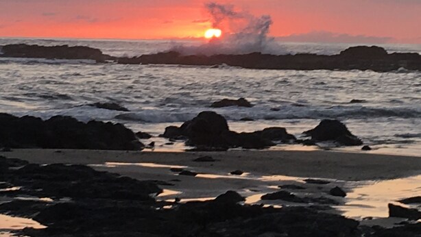 Un atardecer sobre una costa rocosa con olas rompiendo contra las rocas.