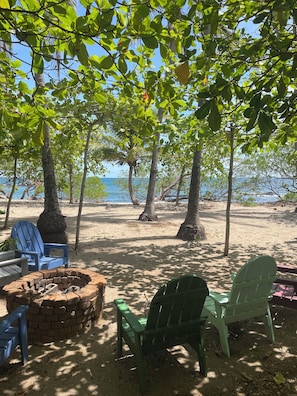 A beachside seating area with chairs and a fire pit, surrounded by trees and overlooking the sea.