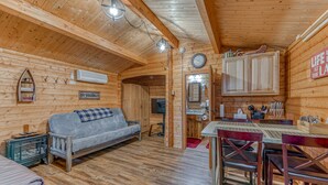A cozy cabin interior with a sofa, dining table, chairs, a kitchen area, and a clock on the wall. - Authentic German Log Cabin in Hayward!! (Hayward)