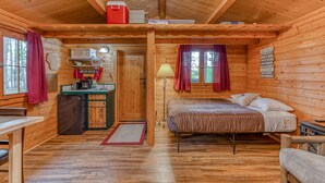 A cozy cabin with a wooden interior, a bed, a desk with a refrigerator, and a window with curtains. - Authentic German Log Cabin in Hayward!! (Hayward)