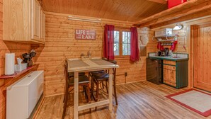A wooden cabin interior with a dining table, chairs, a refrigerator, a kitchen area with a sink and stove, and a sign that reads "Life is better at the lake." - Authentic German Log Cabin in Hayward!! (Hayward)