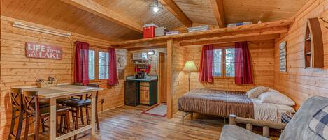 A cozy cabin interior with a wooden dining table, a bed, and a sofa.
