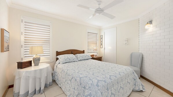 Une chambre à coucher comprenant un lit, une table de chevet, une chaise, un bureau et un ventilateur de plafond.