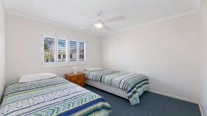A bedroom with two beds, a ceiling fan, and a window with blinds.