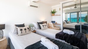 A hotel room with two beds, a desk, a chair, a large mirror, and a view of the sea. - A Point of View - Airlie Beach (Airlie Beach)