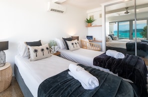 Ett hotellrum med två sängar, ett skrivbord, en stol, en stor spegel och utsikt över havet.