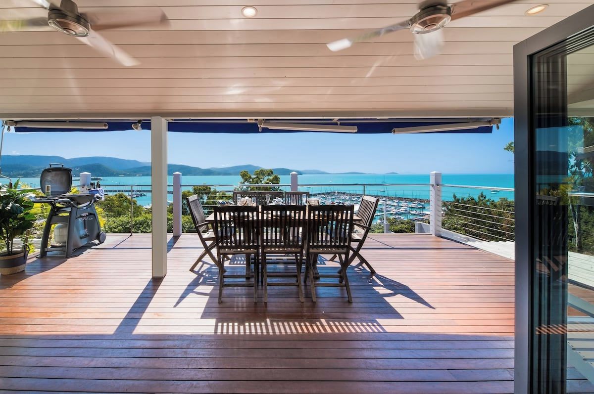 A covered outdoor area with a table and chairs, overlooking a coastal view.