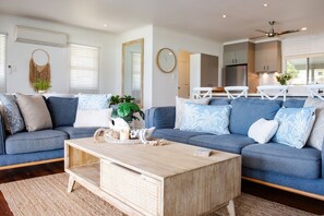 A modern living room with a sectional sofa, a wooden coffee table, and a kitchen in the background. - A Point of View - Airlie Beach (Airlie Beach)