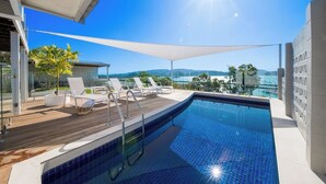 A swimming pool with a wooden deck, lounge chairs, and a view of the ocean. - A Point of View - Airlie Beach (Airlie Beach)