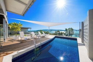 En pool med ett trädäck, solstolar och utsikt över havet.