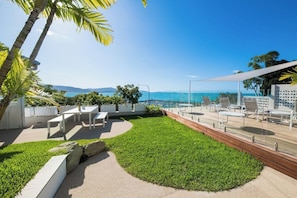 A rooftop terrace with outdoor seating, a view of the ocean, and a clear sky.