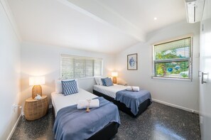 A room with two beds, each with a blue bedspread, a bedside lamp, and a small wicker side table. - A Point of View - Airlie Beach (Airlie Beach)